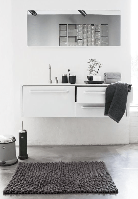 a minimalist neutral bathroom with a floating vanity with storage, a long mirror, grey linens and simple decor