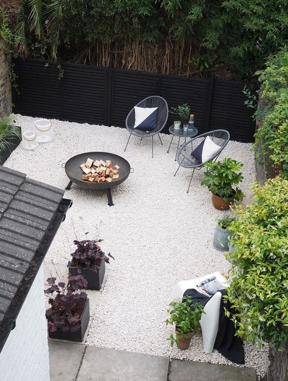 a minimalist patio with black wicker chairs, a black fire bowl, a coffee table and some greenery in pots
