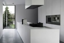 a minimalist white kitchen with sleek cabinets, a long kitchen island and a large hood plus black appliances built-in