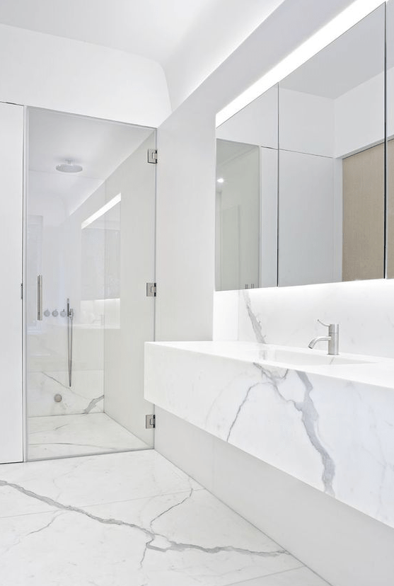 a minimalist white marble bathroom with a shower space, a floating vanity, a statement mirror and built-in lights