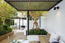 a modern backyard with a dining space, a built-in wooden bench and a white table plus lots of greenery planted