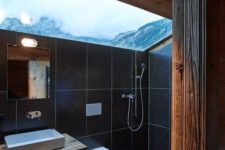 a modern chalet bathroom done with light-colored wood and black tiles and with a skylight to enjoy the views
