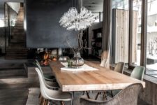 a modern chalet dining space with a wooden table, catchy chairs, a gorgeous bulb chandelier and a fireplace