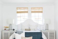 a modern coastal bedroom with wicker shades, a white bed and perforated nightstands, a blue sofa and printed bedding