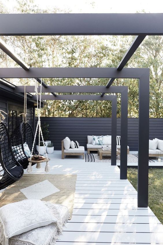 a modern monochromatic patio with black pendant chairs, boho pillows, simple wooden furniture with printed pillows