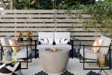 a modern patio with a concrete fire pit, comfy chairs and a sofa, printed textiles in black and white and lights