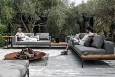 a modern patio with comfy grey sofas, a large fire pit, a white deck and trees around the space