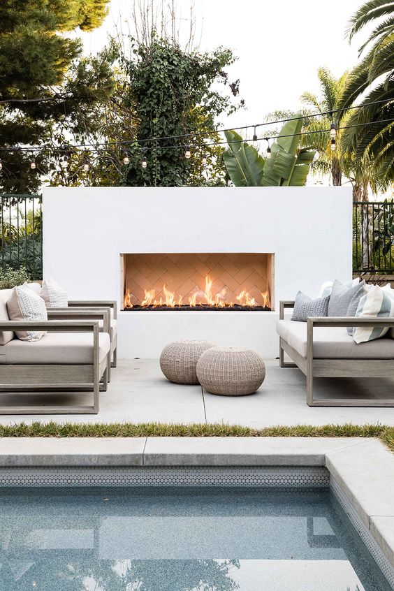a modern patio with neutral furniture, a white built in fireplace and wicker ottomans is welcoming