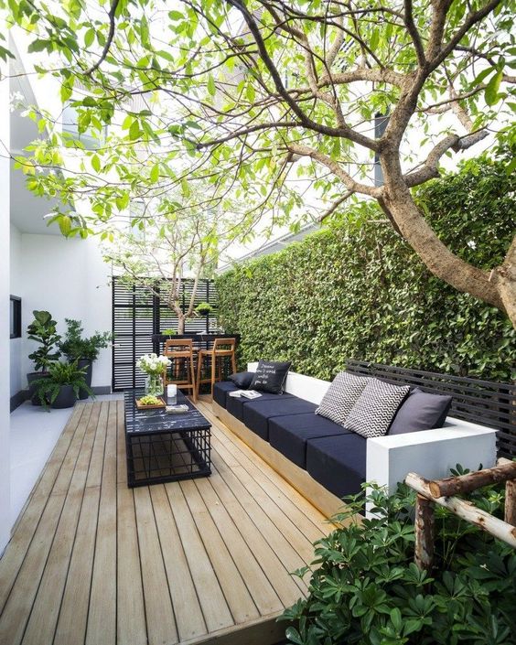 a modern welcoming backyard with a deck, s amll bar space, a large sofa and a black coffee table plus a living wall