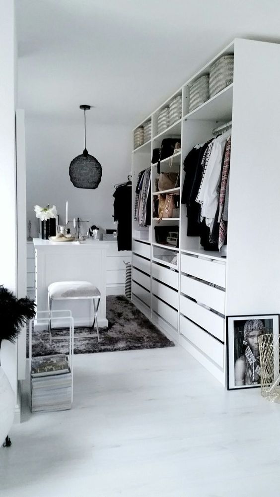 a monochromatic minimalist closet with a large storage unit with drawers, open compartments and a white vanity plus a stool