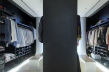 a moody minimalist closet in black and navy, white benches, holders, open and closed shelves plus built-in lights