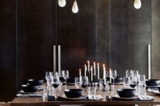 a moody modern chalet dining space with black walls, dark modenr furniture, a catchy chandelier and candles