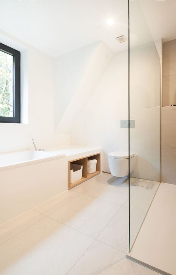 a neutral minimalist bathroom with a window, a tub with storage, a floating toilet and a shower plus lots of light