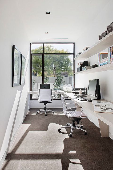 a neutral minimalist home office with a double floating desk, open shelves, artworks and comfortable chairs