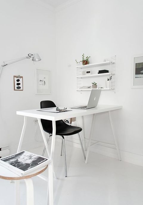 a pure and airy minimalist white home office with a trestle desk, an open shelf, artworks, a lamp and stools