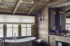 a refined chalet bathroom clad with reclaimed wood, with printed tiles, a metal tub, a built-in vanity, vintage stools and chairs
