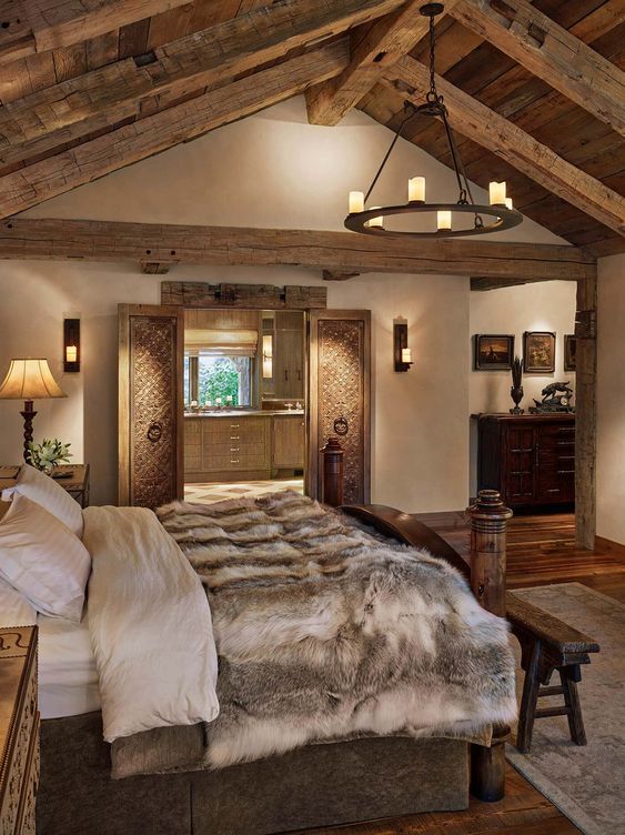 a refined chalet bedorom with carved wooden furniture, a candle chandelier, lots of lamps and faux fur