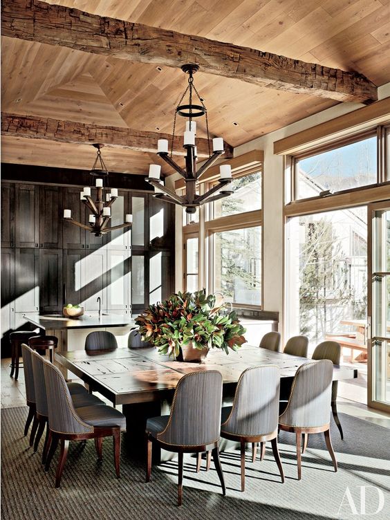 a refined chalet dining room with a large wooden table, mid-century modern chairs, statement chandeliers