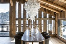 a refined chalet dining room with a metal table, woven chairs, a statement chandeleir and gorgeous views