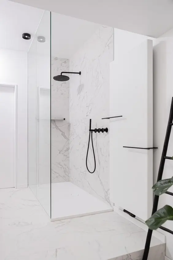 a refined minimalist bathroom done with white marble, a shower space, black fixtures and lots of light