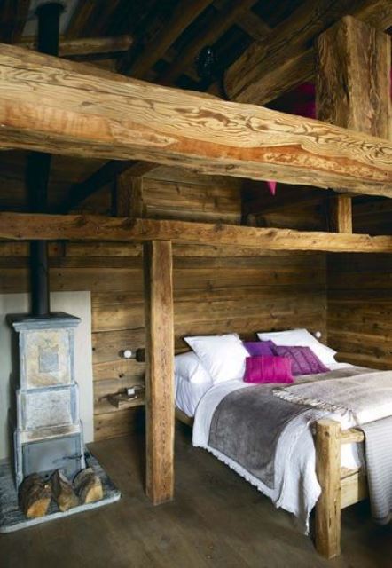 a small chalet bedroom with wooden beams and wooden furniture, a small hearth and colorful bedding