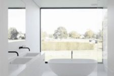 a small minimalist bathroom in white, with a glazed wall, a flaoting vanity, a free-standing tub and a large mirror