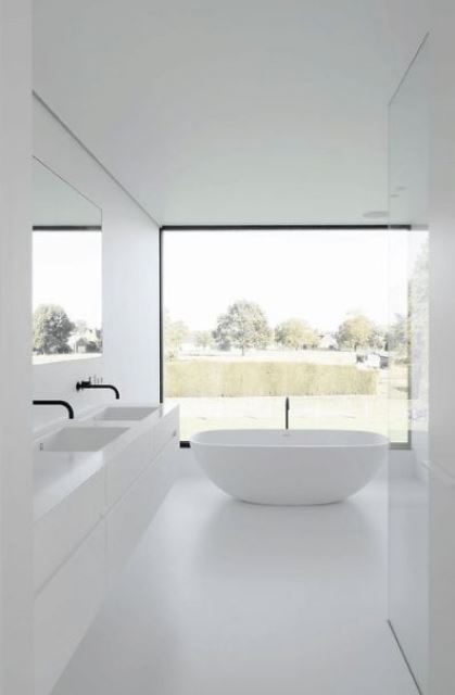 a small minimalist bathroom in white, with a glazed wall, a flaoting vanity, a free-standing tub and a large mirror