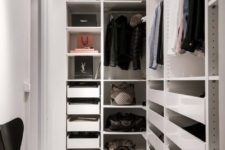 a small minimalist closet with holders for hangers, lots of drawers, open shelves and a single black chair