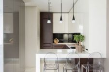 a small minimalist kitchen in white and chocolate brown, wtih a bar, ghost stools and cool pendant lamps