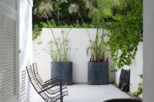 a small minimalist patio with black metal chairs, concrete planters with statement plants and a metal bowl with floating blooms