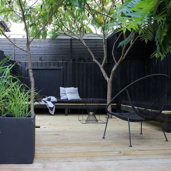 a stylish monochromatic backyard with a logn black bench, black chairs and a fire pit plus some trees in here
