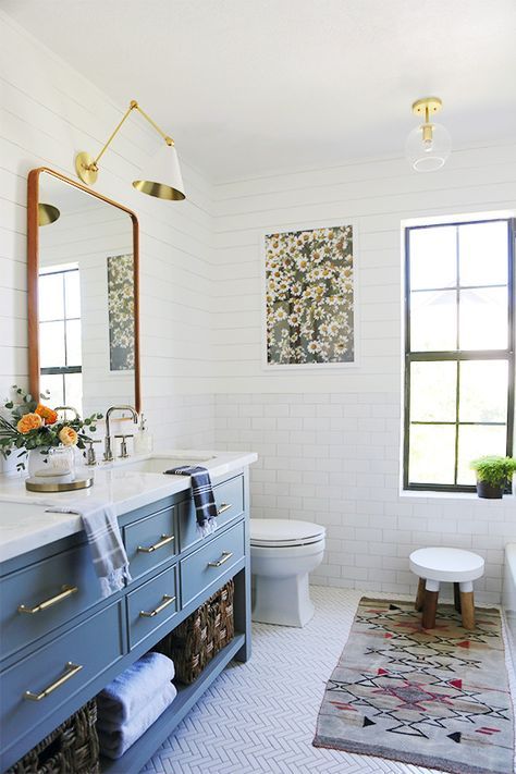 a sweet farmhouse bathroom clad with white subway tiles, with a blue vanity, a mirror and gold lamps and sconces