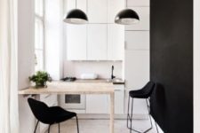 a tiny monochromatic kitchen with sleek white cabinets, a black accent wall, a bar and black stools plus black pendant lamps