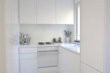 a tiny white minimalist kitchen with sleek cabinets, white countertops and a backsplash looks larger than it is