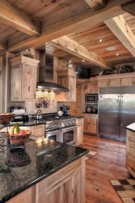 a traditional chalet kitchen all clad with wood, with black stone countertops, a tile backsplash and metal appliances and built-in lights