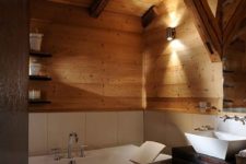 a welcoming chalet bathroom with a dark vanity, clad with wood and white tiles, with lamps and a free-standing tub