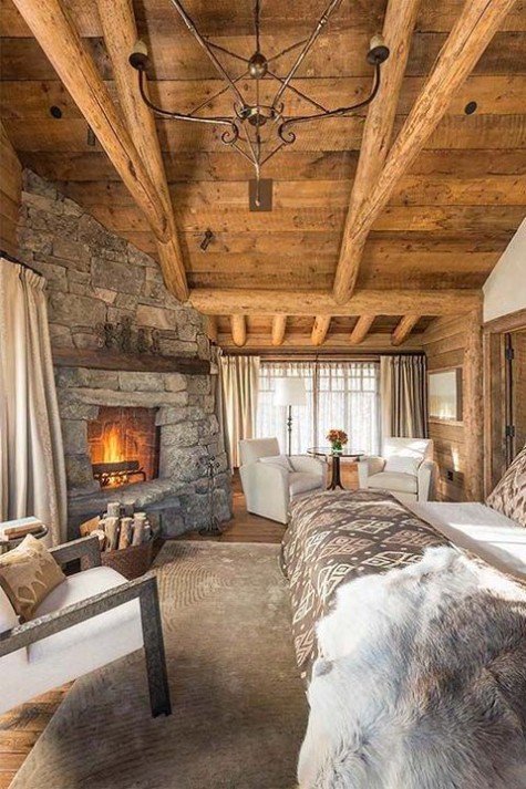 a welcoming chalet bedorom clad with wood, with a stone fireplace, faux fur and a sitting zone by the fire