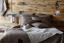 a welcoming chalet bedroom clad with light stained wood, with candle lanterns, dark bedding and some pretty decor