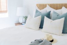 a welcoming coastal bedroom with a wicker bed, blue pillows, woodne nightstands and wicker shades