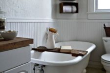 a white farmhouse bathroom with wallpaper and beadboard walls, a vintage tub, wooden box shelves and a vanity