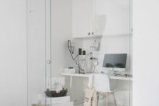 a white minimalist home office with a desk, a storage unit, a white chair and some boxes plus glass sliding doors