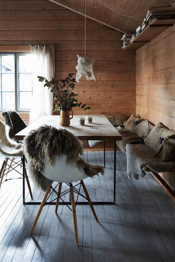 an eclectic chalet dining room with a corner bench with faux fur and pillows, a modern table and chair with fur