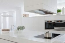 an elegant minimalist white kitchen with lots of cabinets, a large stone clad kitchen island and a large hood over it