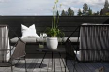 an ultra-minimalist terrace with a wooden deck, black wicker chairs, a black coffee table and some neutral textiles