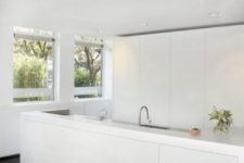 an ultra-minimalist white kitchen with sleek tall cabinets and a large kitchen island plus a raised top for eating here