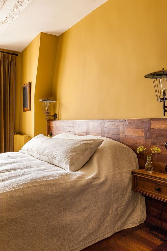 a rustic bedroom with warm yellow walls, a wooden bed and nightstands and heavy mustard curtains