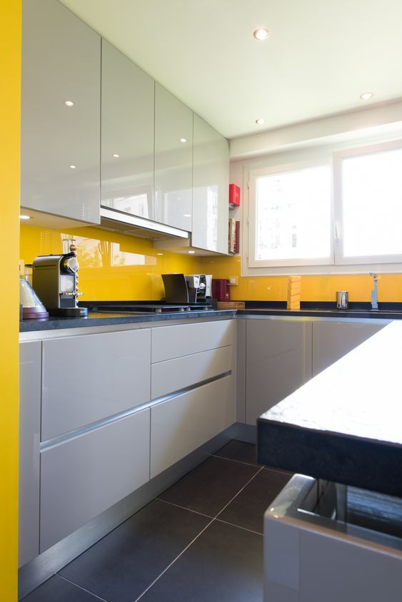 a minimalist kitchen with dove grey and grey minimal cabinets and a sunny yellow glass backsplash