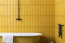 18 a minimal bathroom with mustard tile walls and a mustard bathtub, a dark stone tile floor and baskets
