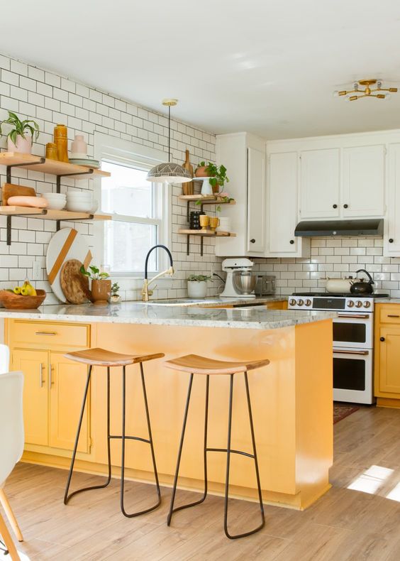 a neutral boho ktichen with white upper cabinets, yellow lower ones that add color and warmth to the space