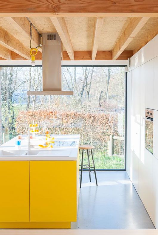 a white contemporary kitchen with a glass wall and a sunny yellow kitchen island for a colorful statement